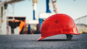 A bright hard hat sitting on the asphalt in the foreground of a construction site